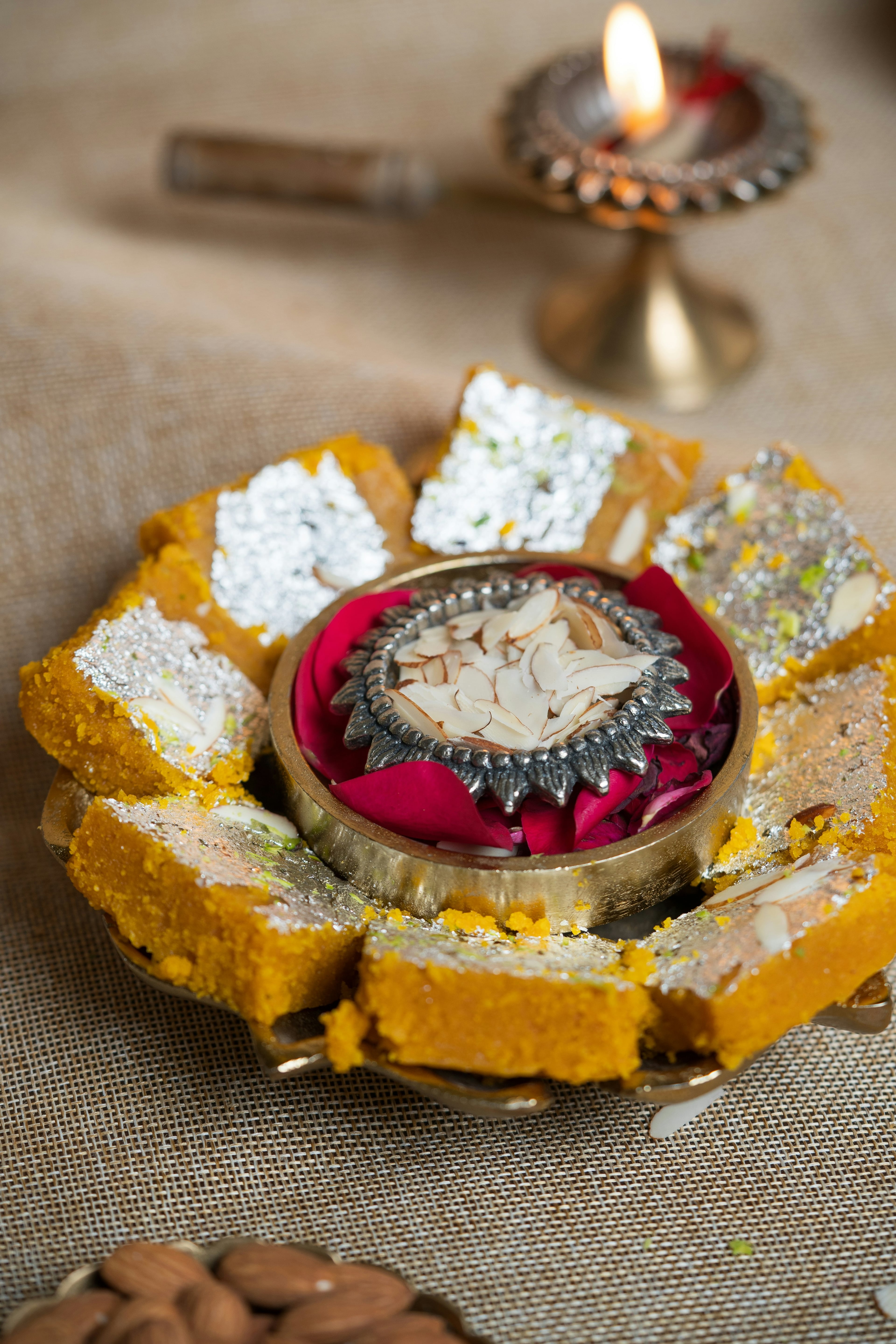 Indian sweets on a tray, an oil lamp lit behind them
