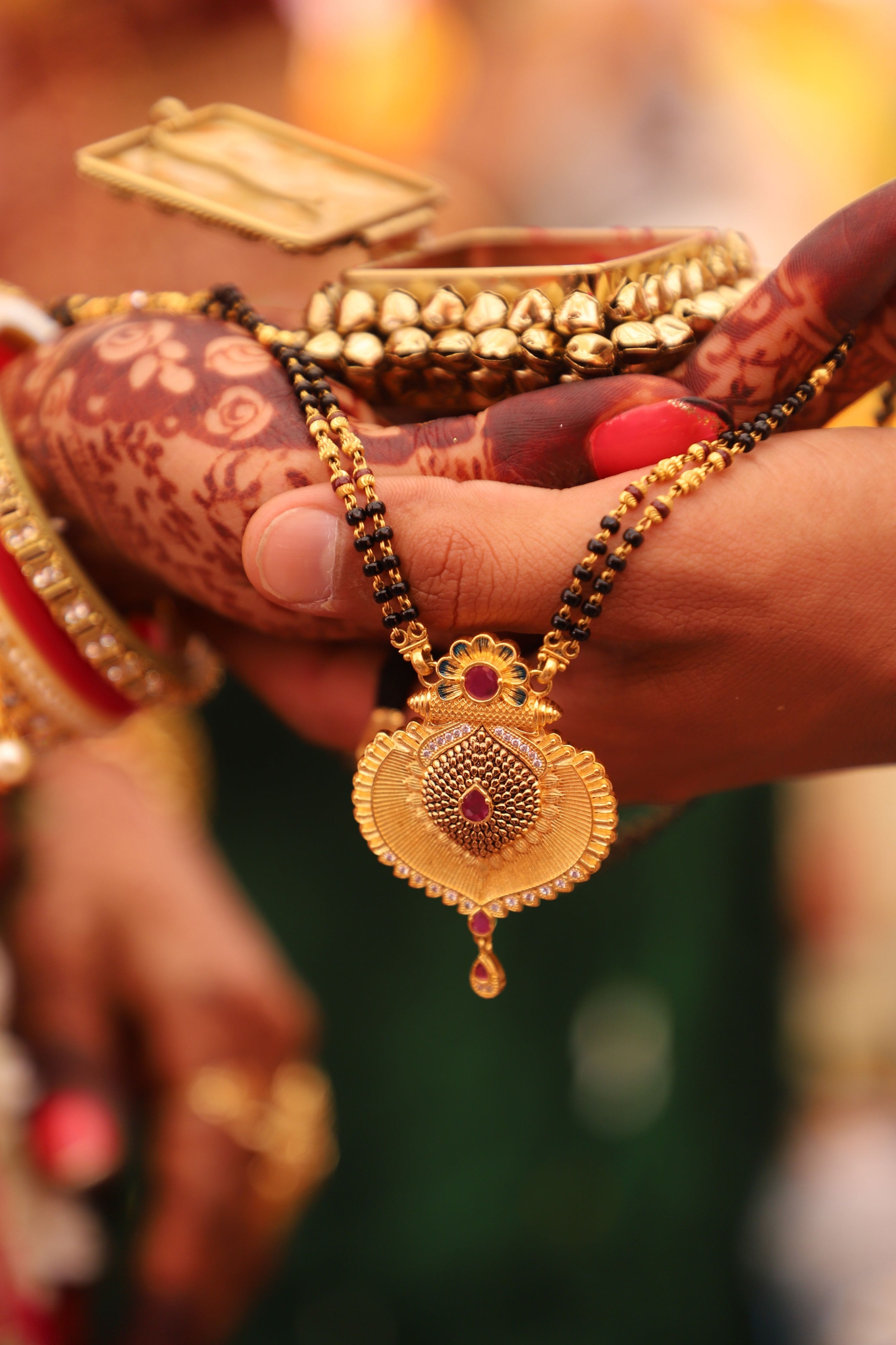 A gold and black-bead mangalsutra held between hands painted with henna