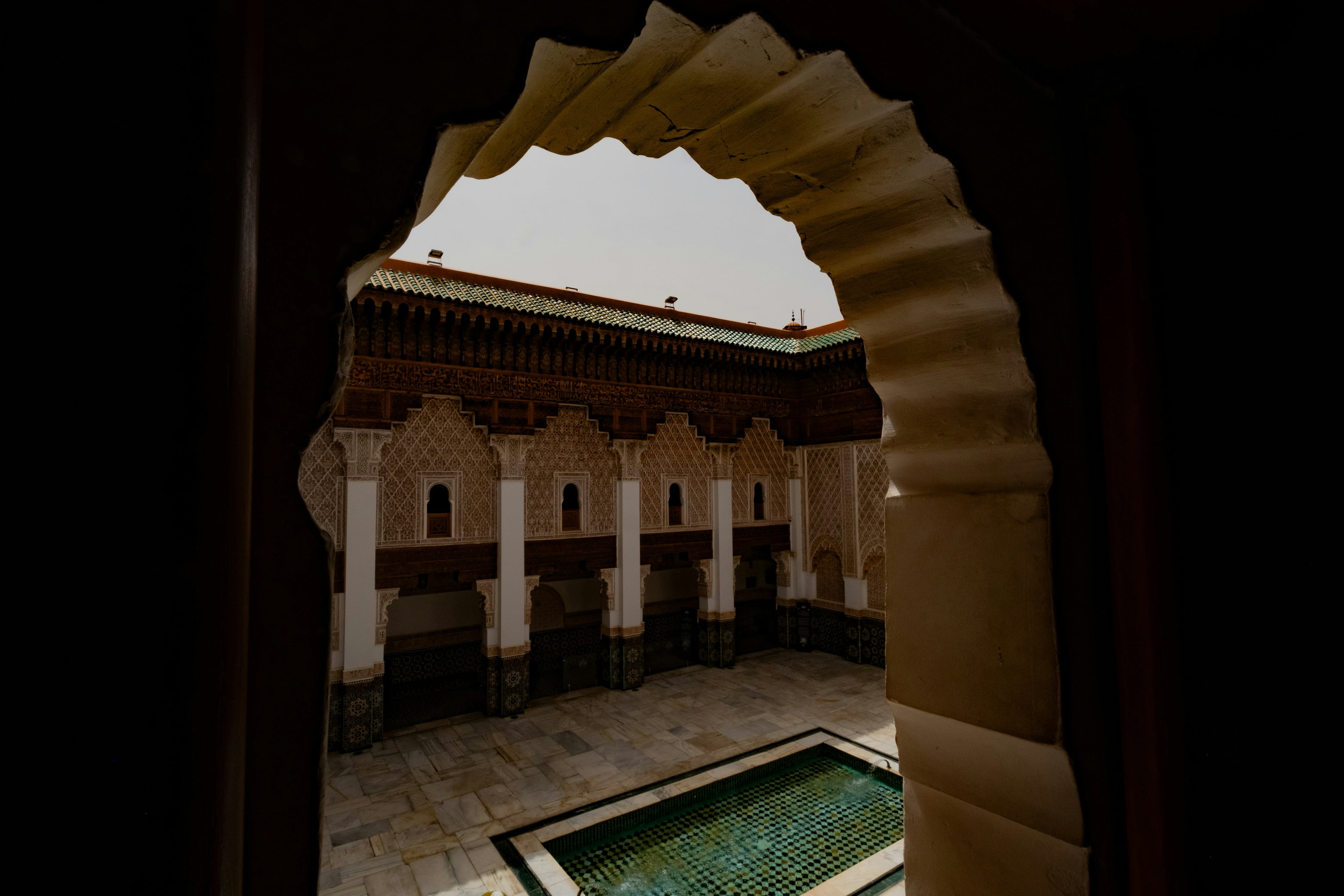 A madrasa courtyard and its pool seen through a carved arch, Marrakech