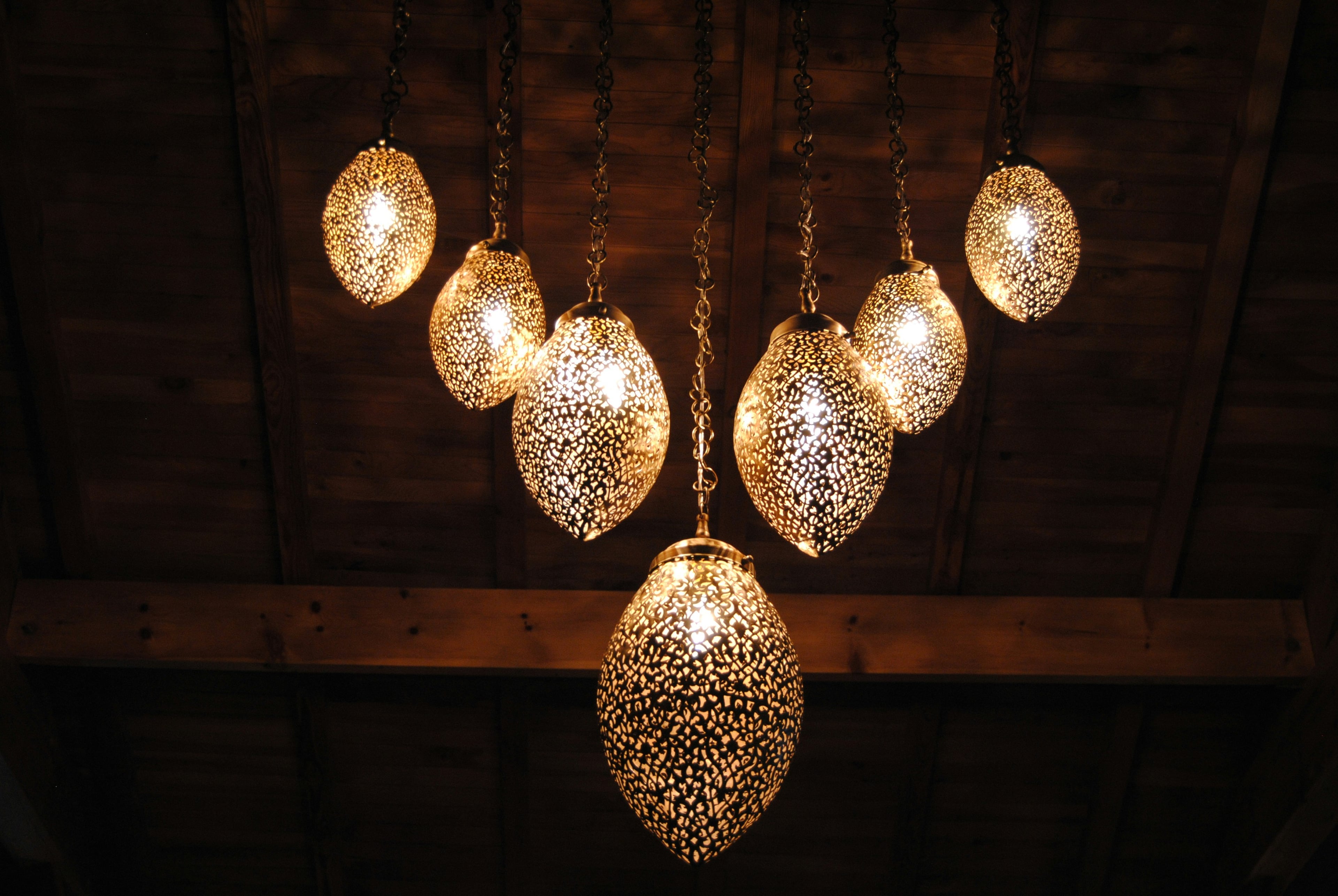 Pierced brass pendant lamps glowing under a wooden ceiling