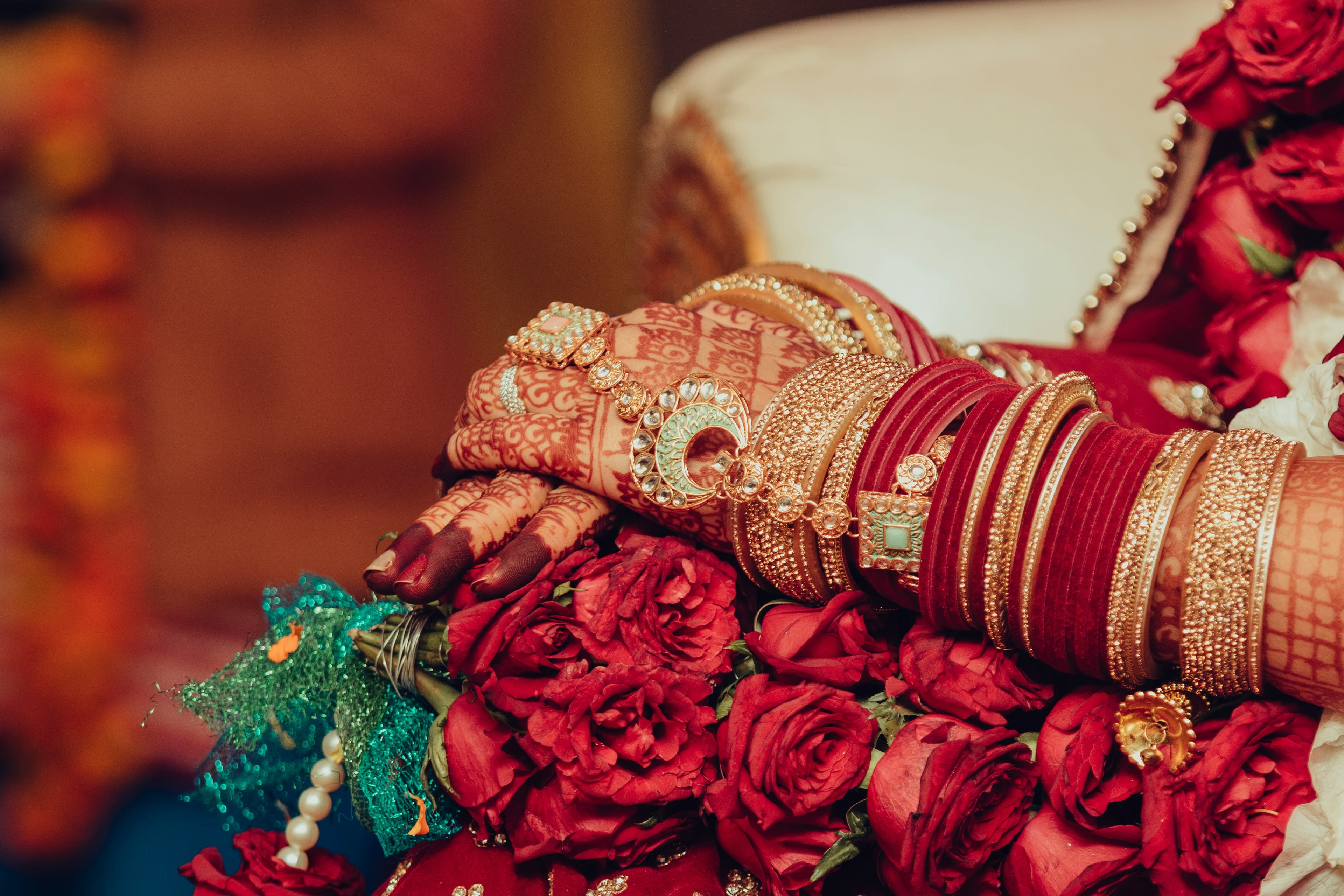 A bride's hands with henna, red and gold bangles and a bouquet of red roses