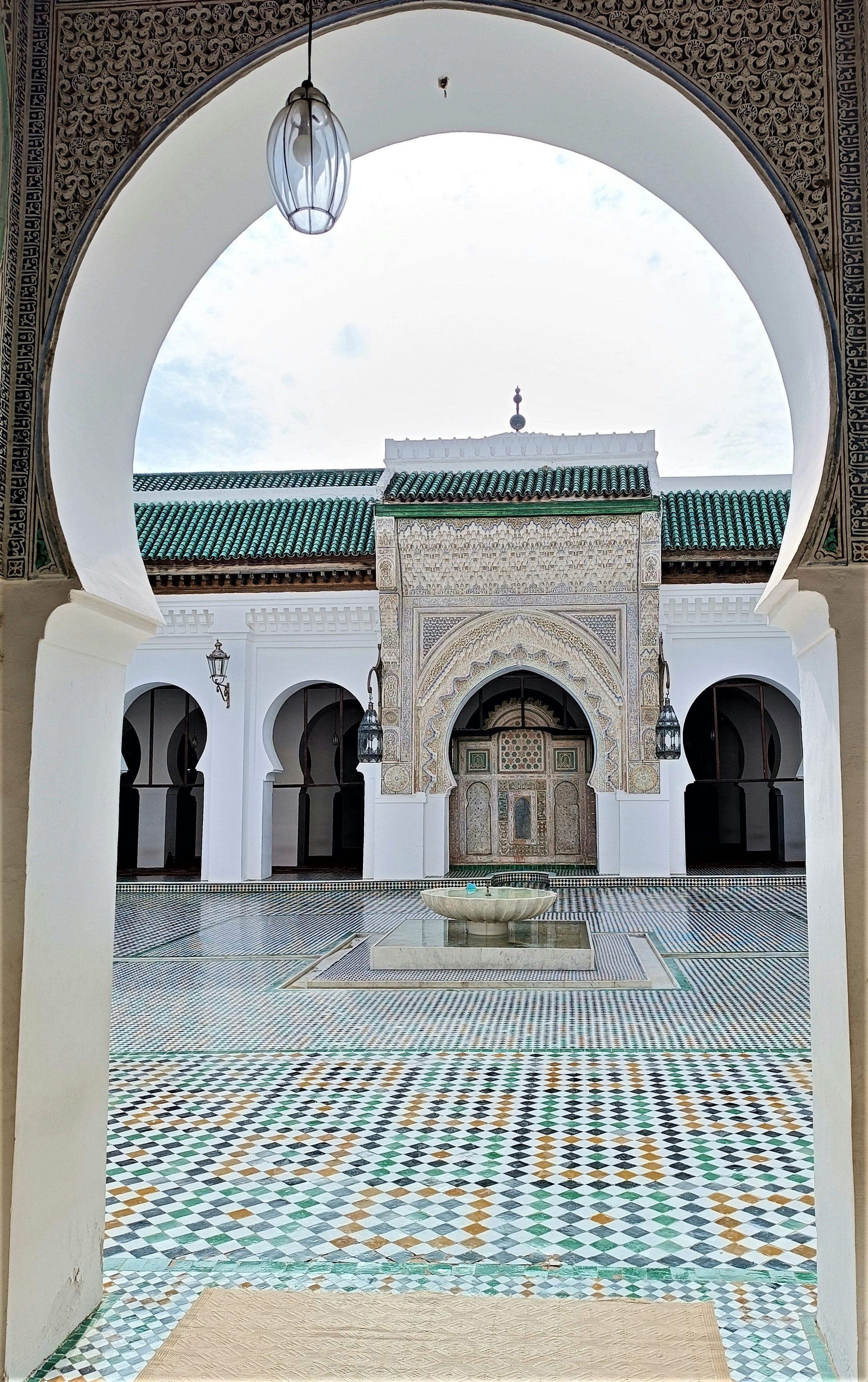 A courtyard paved with zellige, seen through a white arch, Fès